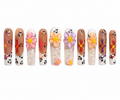 Long square press-ons layer warm brown and nude tones with leopard print accents, colorful starburst nail art in orange, pink, and purple, raised 3D flowers in pink, peach, and lavender, iridescent crystal flake fills, and swirling orange and purple details.