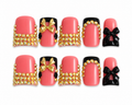 Luxury coral pink square press-on nails with black 3D bows, gold rhinestones, glossy finish, and black accent details displayed on a white background.