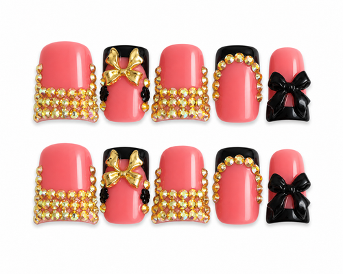 Luxury coral pink square press-on nails with black 3D bows, gold rhinestones, glossy finish, and black accent details displayed on a white background.