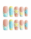 Pastel square press-on nails with blue and yellow gradient designs, 3D flower accents, butterfly nail art, glossy finish, and soft spring-inspired details displayed on a white background.